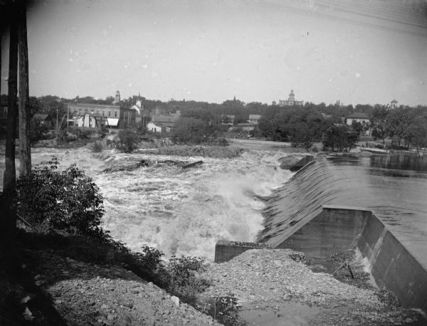 Exterior portrait of the dam in front of Black River Falls with the town in the background. The dam was reportedly constructed in 1906.