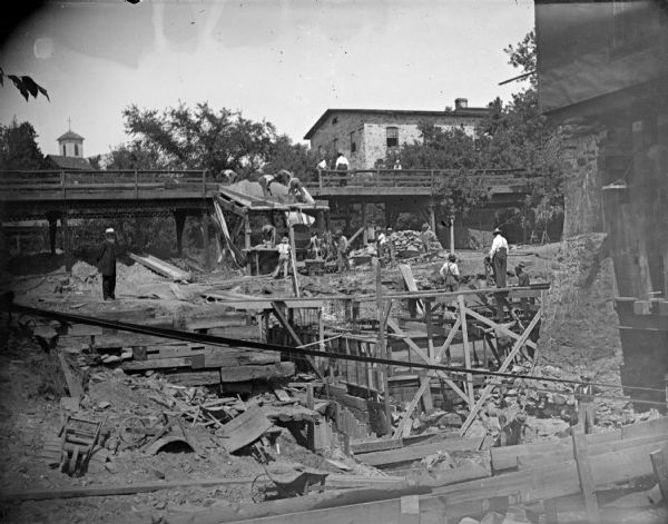 Outdoor view of men working at a construction site. Identified as the construction of the third powerhouse, which also entailed moving the second powerhouse north. Looking west from the German Hill bridge.