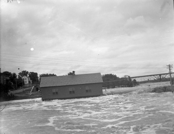 View across water towards a powerhouse among very high water on the Black River. Identified as the second power house with high water in 1905.
