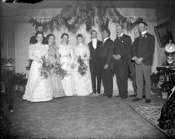 Interior group portrait of parties in a wedding, including four women and five men.