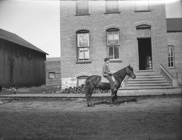 View across street towards a boy posing sitting in profile on a horse in front of the building at 13 South First Street, which held the photography studio of Charles Van Schaick.