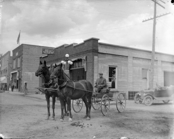 Outdoor view of a man sitting in a wagon pulled by a team of horses at the intersection of First and Harrison Streets, with the northeast corner visible in the background, and probably a Ford Model "T" automobile. Taken after the 1911 flood.