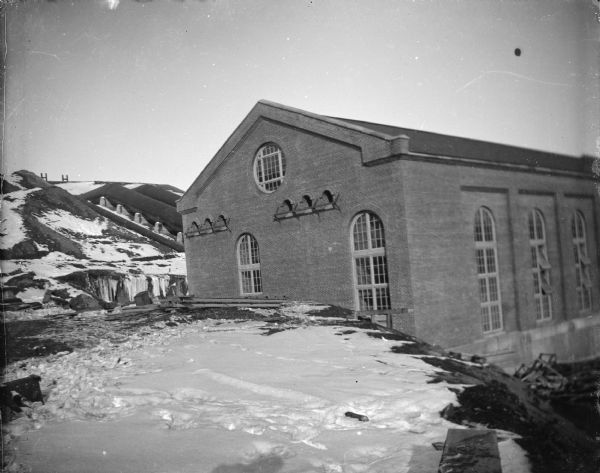 Outdoor view across snow-covered ground towards a large brick building surrounded. There is a hill in the background. Location identified as the powerhouse on the canal in Hatfield.