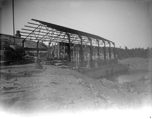 Outdoor view of the construction of a large building on top of a dam. Location identified as the construction of the powerhouse on the canal in Hatfield.