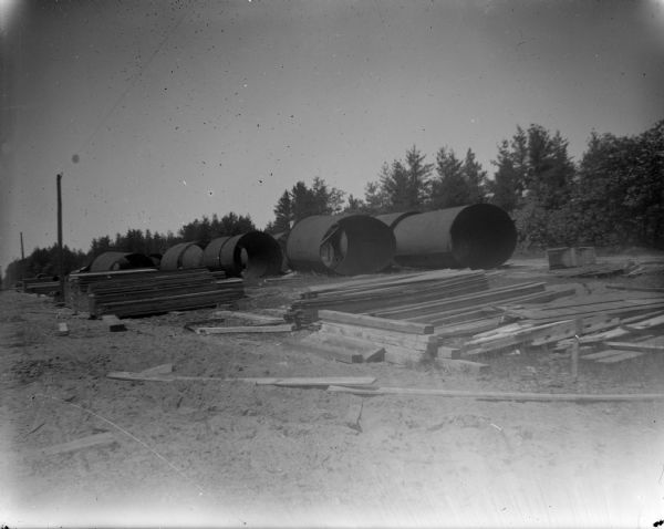 Outdoor view of a construction site of large pipes and other building materials. Identified as the construction site of the powerhouse at the Hatfield dam in 1907.