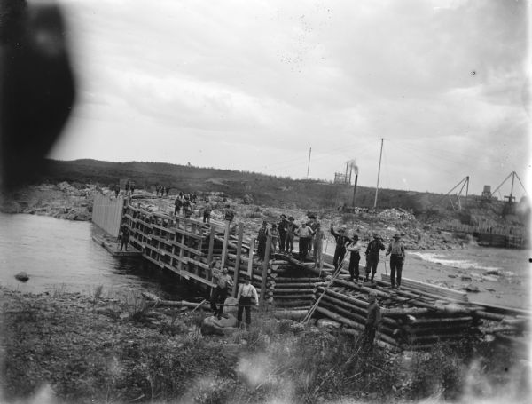 Slightly elevated view of men working on the construction of a dam across a river. Identified as the construction of the Hatfield Dam in 1907.