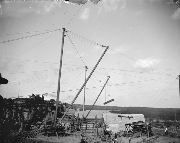 Exterior portrait of the construction site of a dam on a river. Identified as the construction of the Hatfield dam in 1907.