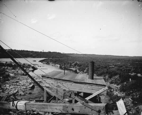 Elevated view of the construction site of a dam on a river. Identified as the construction of the Hatfield dam in 1907, looking north up the Black River.