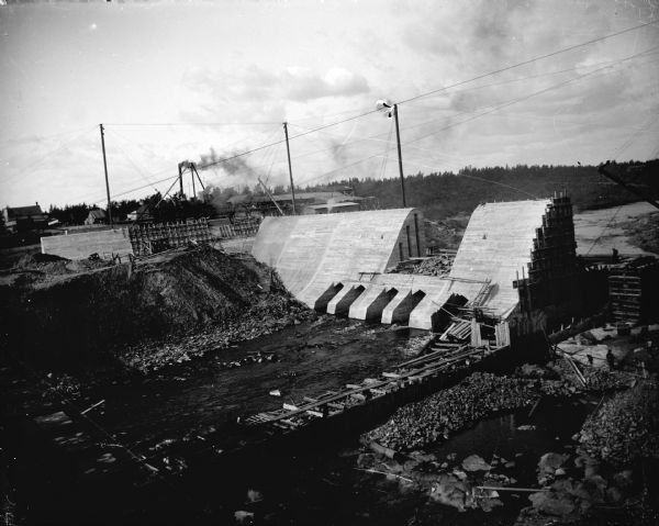 Elevated view of the construction site of a dam across a river. Identified as the construction of the Hatfield dam across the Black River in 1907.