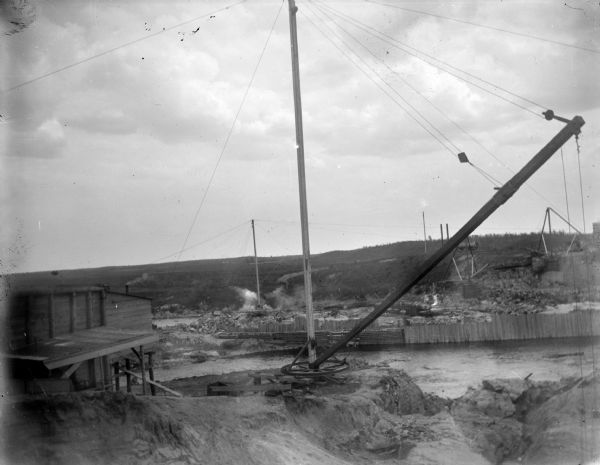 View looking down towards the construction site of a dam across a river. Identified as the construction of the Hatfield dam across the Black River in 1907.