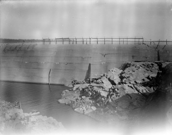 View looking up towards a dam across a river with a rocky shoreline. Identified as the Hatfield dam across the Black River.