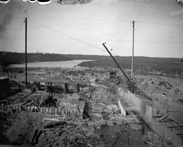 Elevated view of the construction site of a dam across a river. Identified as the construction of the Hatfield dam across the Black River in 1907 to 1909.