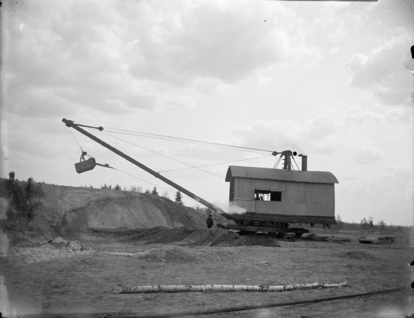 A steam dredge at the construction site of a dam on a river. Identified as the construction of a canal at the Hatfield dam construction in 1907.