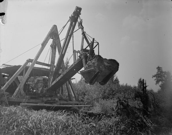 A walking dredge in action in a cranberry marsh. Probably the walking dredge at Gebhardt Marsh mentioned in the obituary of C.J. Van Schaick, and in the Badger State Banner Semi-Centennial Anniversary.