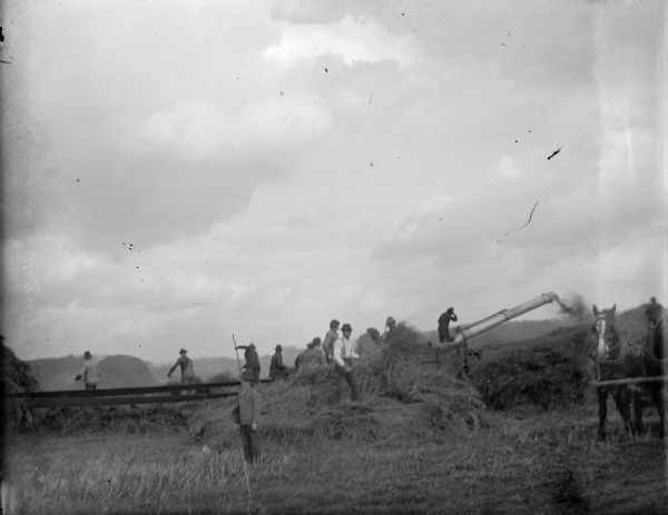 View across field towards a group of men working with threshing machinery.