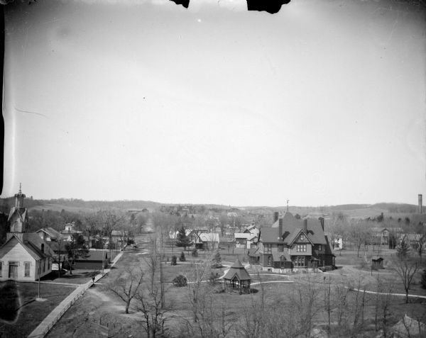 Elevated view of a cityscape. Identified as probably the city of Black River Falls from the Jackson County Courthouse, looking west, showing the Catholic Church and the Price house on Tyler Street.