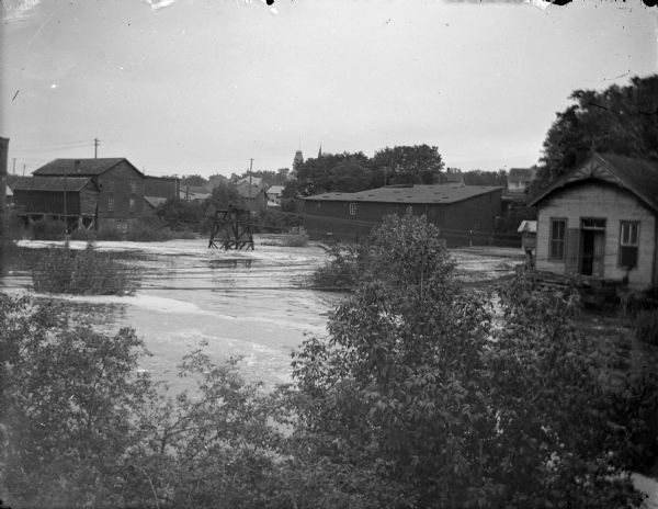 Elevated view towards high water in a town. Location identified looking west from the German Hill bridge in Black River Falls. The high water is from a flooded Town Creek. The feed mill is located on the left, the starch factory located right center, and the powerhouse is located on the right at the end of the power lines.