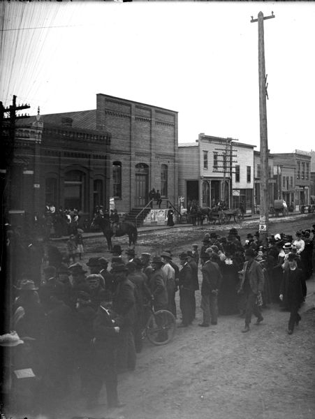 Elevated view of a large group of people lining a city street. Location identified the south side of Main Street between First and Second Streets.