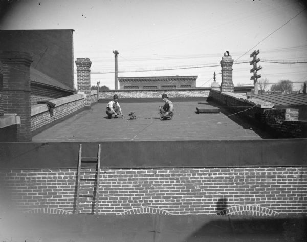View of men working on top of a roof. Location identified as the roof of the Tomter Building at 106 Main Street in Black River Falls, which was a bank, post office, dry cleaner, and abstract office (1974). Probably taken from the photographic gallery window of Van Schaick.