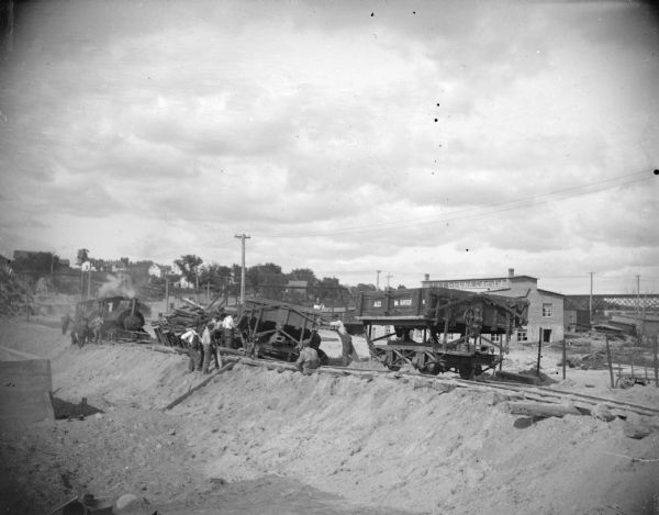 View towards a construction site, with a railway track with a train and other machinery. Location identified as the fill and reconstruction of Town Creek after the 1911 flood in Black River Falls.