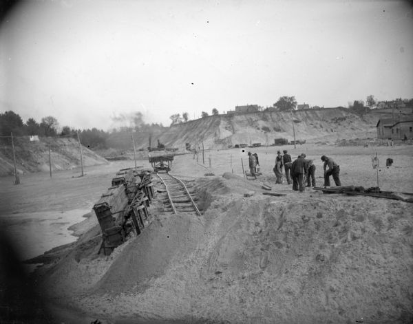 View towards a construction site, with wreckage, and men working on the right. Location identified as the fill and reconstruction of Town Creek after the 1911 flood in Black River Falls, and the wreck of the sand hauler.