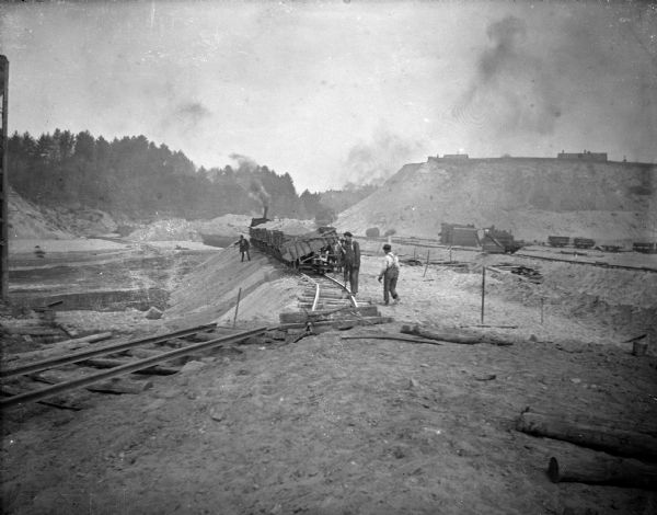 View towards a construction site, with men working near a railway track with sand haulers. Location identified as the fill and reconstruction of Town Creek after the 1911 flood in Black River Falls.