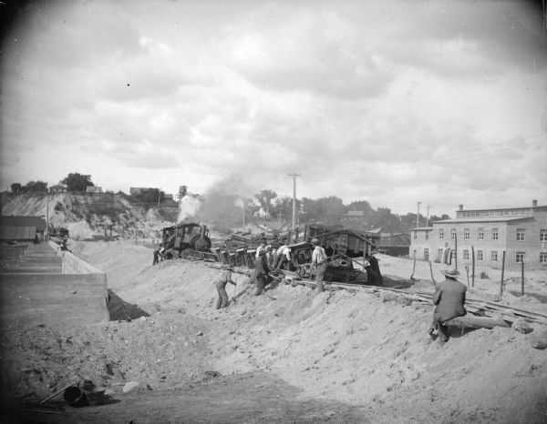 View towards a construction site, with men working by a railway track with sand haulers, and a brick viaduct. Location identified as the fill and reconstruction of Town Creek after the 1911 flood in Black River Falls.