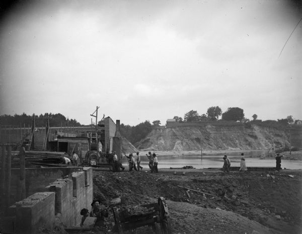 View towards a construction site, with people walking on a dirt road, and others working at the site. Location identified as the reconstruction following the flood in Black River Falls in October 1911.