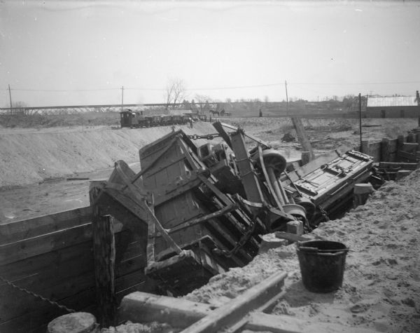 View of a construction site with wreckage in a ditch. Location identified as the fill and reconstruction of Town Creek after the 1911 flood in Black River Falls, and the wreck of the sand hauler.
