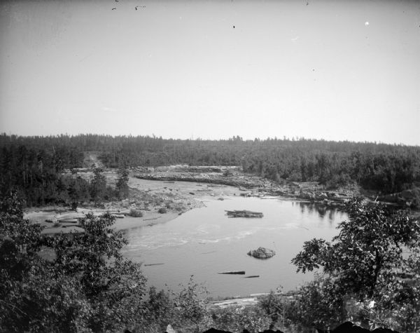 Elevated view of a body of water with frost on the banks. Identified as the Black River. Logs are along the shore.