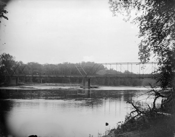 View from shoreline towards a bridge across a body water. Identified as probably the bridge across the Black River at Melrose.