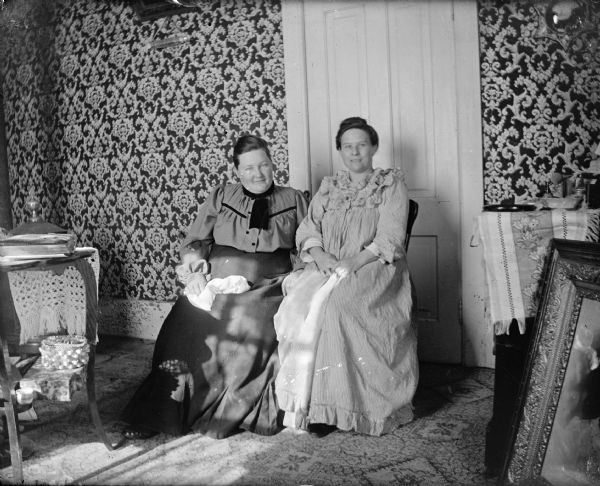 Portrait of two women posing sitting in front of a door.