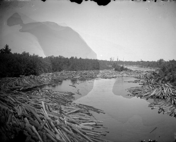Outdoor view of large groups of logs along the shores of a body of water. Identified as the Black River.