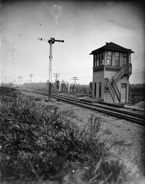 View across railroad tracks towards a railroad signal tower. Location identified as the signal tower for the Sheppard's cut-off south of Black River Falls.