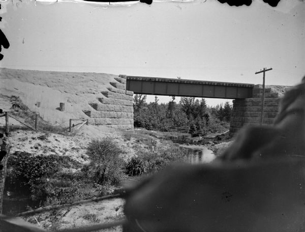 View along riverbank towards a railroad bridge. Location identified as Levi's Bridge.