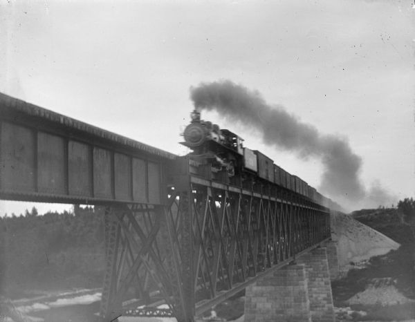 View towards a train coming over a bridge. Identified as a railroad bridge in Black River Falls after 1903.