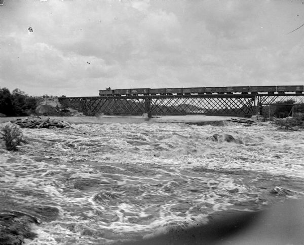 View across water towards a train crossing a railroad bridge across a river.
