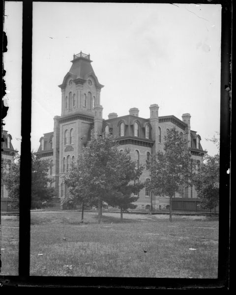 View across lawn towards a large brick building. Identified as the Union High School built in 1871 in Black River Falls. The is the right image of a split stereo photograph.