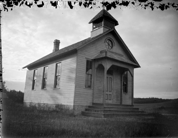 View across lawn towards a small wooden school house in a field. The school is the Spring Creek School to the south of Black River Falls.