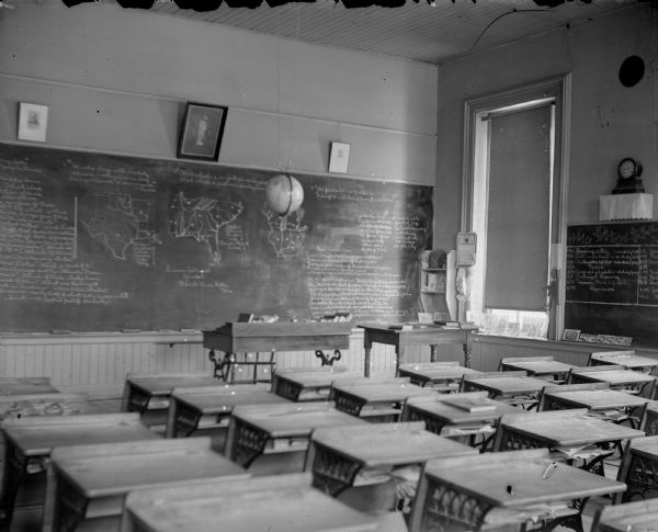 View from back of room towards the front of a classroom. Identified as a room in the school building built in 1872 in Black River Falls.
