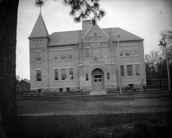 View across street towards the front of a large brick school building. Identified as the high school built in 1897 in Black River Falls.