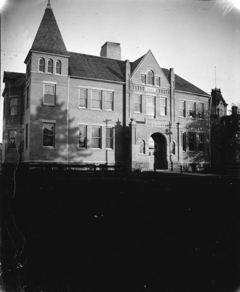 View across lawn towards a large brick school building. Identified as the high school built in 1897 in Black River Falls.