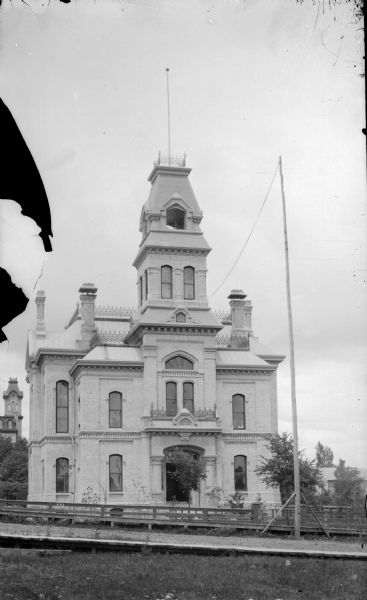 View across lawn and street towards a large building. Identified as the Jackson County Courthouse in Black River Falls.