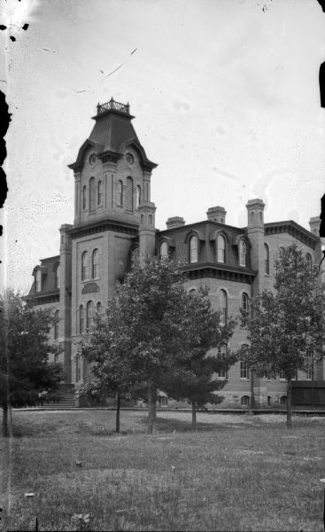 View across lawn towards a large brick building. The building is identified as the Union High School built in 1871 in Black River Falls.