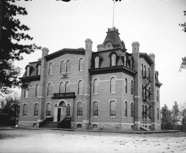 View across grounds towards a large brick building, which is identified as the school building built in 1872.