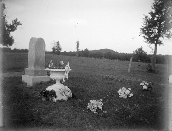 View of a tombstone, an urn with flowers, and three other flower arrangements in a cemetery.