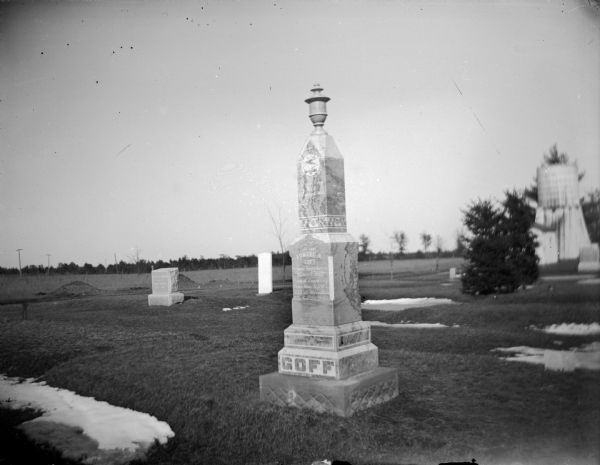 View of the front of a tombstone in a cemetery. Identified as the memorial for Edward N. Goff in the Black River Falls Cemetery. There are patches of snow on the ground.