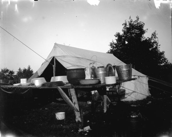 View of a table with buckets, pots, and other objects on top of it in front of a tent.