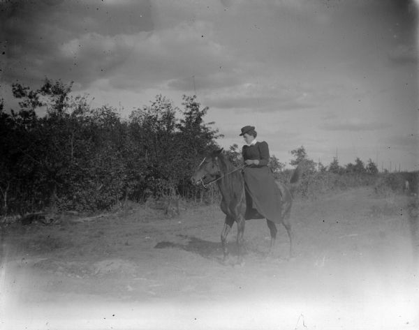 View towards a woman sitting on a horse in a field, with trees in the background.