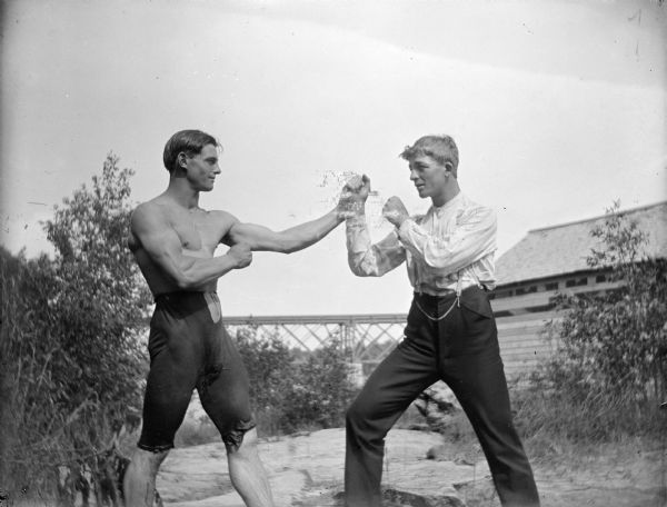 Two men are posing in profile in a fighting stance. Identified as Lutie Frantz on the left, and Elmer on the right.